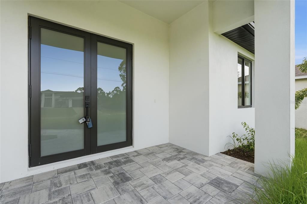 A covered patio features gray paver flooring, white walls, and a dark-framed double glass door — 14041 NEWSON LANE, PORT CHARLOTTE, FL