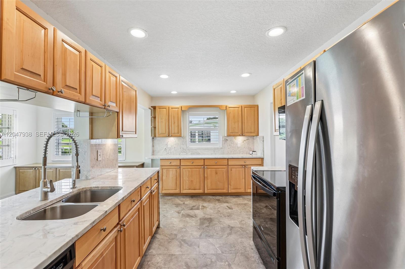 A kitchen features light wood cabinets, marble-look countertops, stainless steel appliances, and gray tile flooring — 8855 NW 10th Pl, Plantation FL 33322, PLANTATION, FL