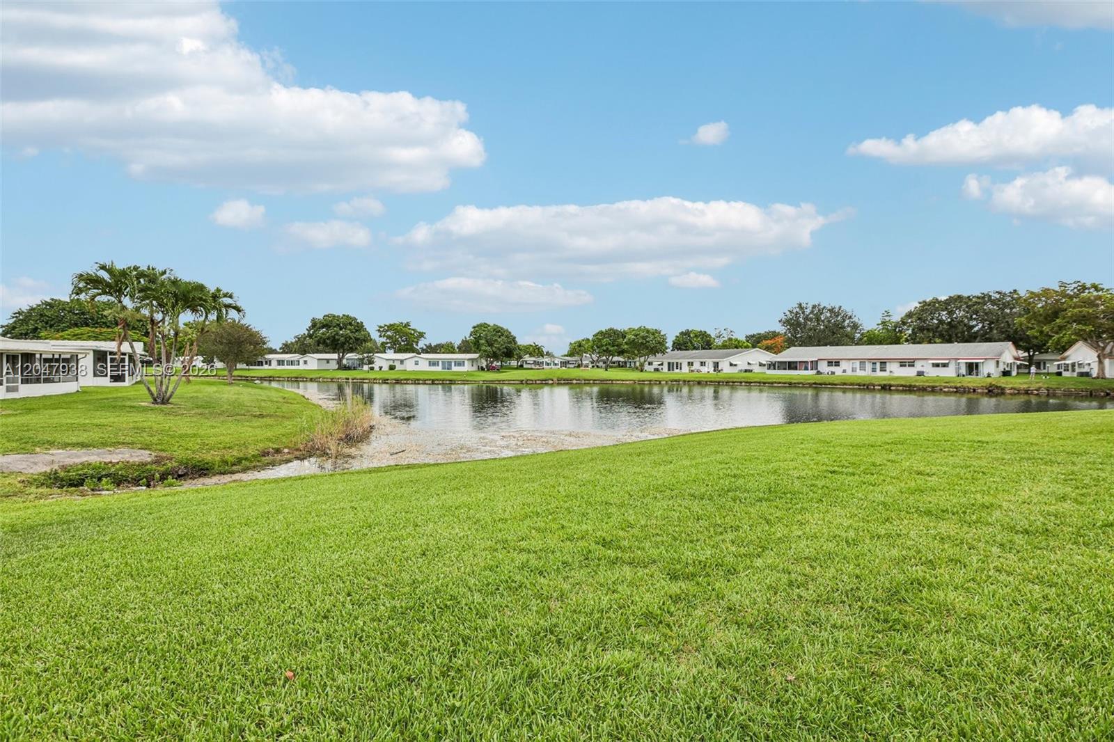A grassy lawn overlooks a small lake surrounded by residential buildings under a blue sky — 8855 NW 10th Pl, Plantation FL 33322, PLANTATION, FL
