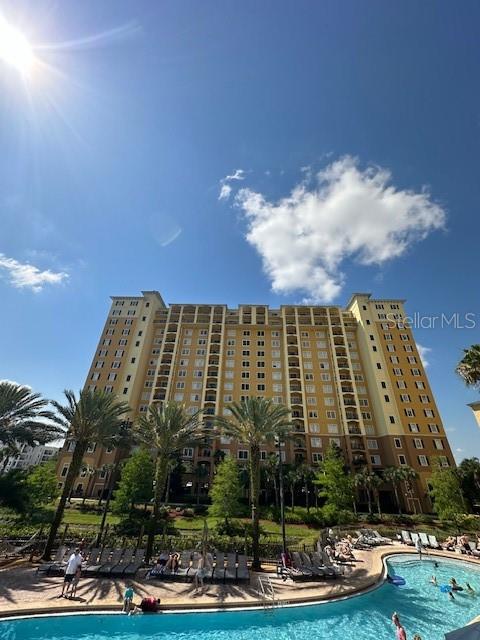 A tall, multi-story apartment building stands behind a swimming pool with lounge chairs and palm trees — 8101 RESORT VILLAGE DRIVE UNIT 3608, ORLANDO, FL