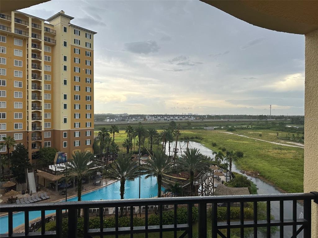 A balcony view overlooking a swimming pool, palm trees, a pond, and a tall apartment building — 8101 RESORT VILLAGE DRIVE UNIT 3608, ORLANDO, FL