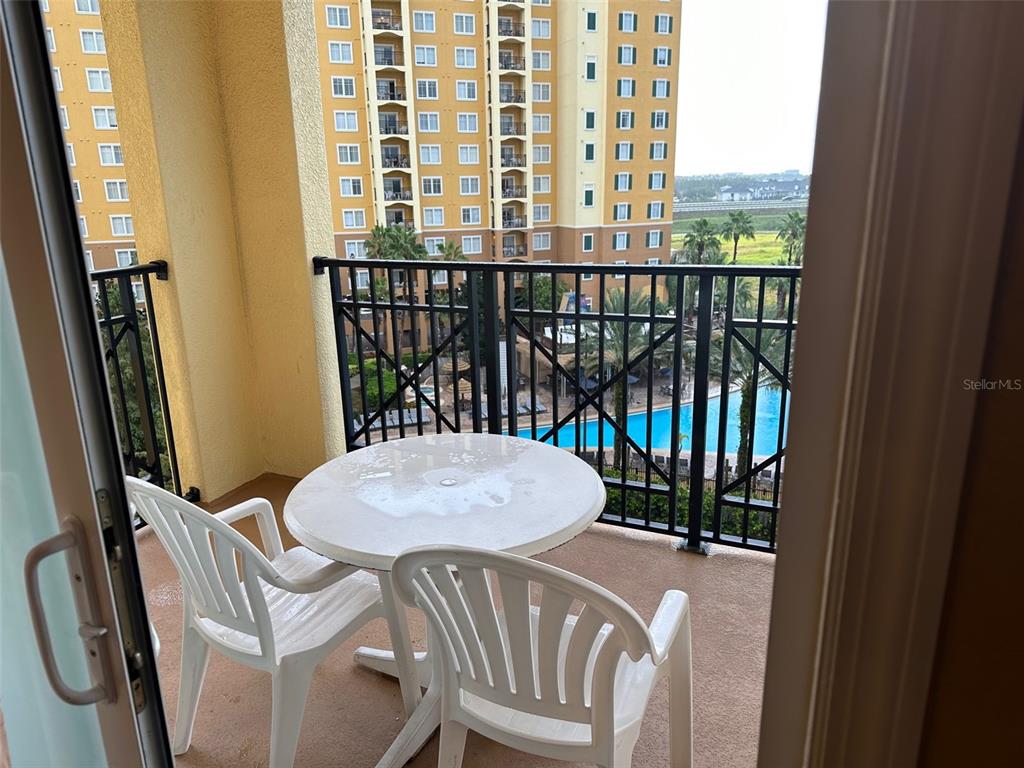 A balcony with a small table and two chairs overlooks a swimming pool and building — 8101 RESORT VILLAGE DRIVE UNIT 3608, ORLANDO, FL