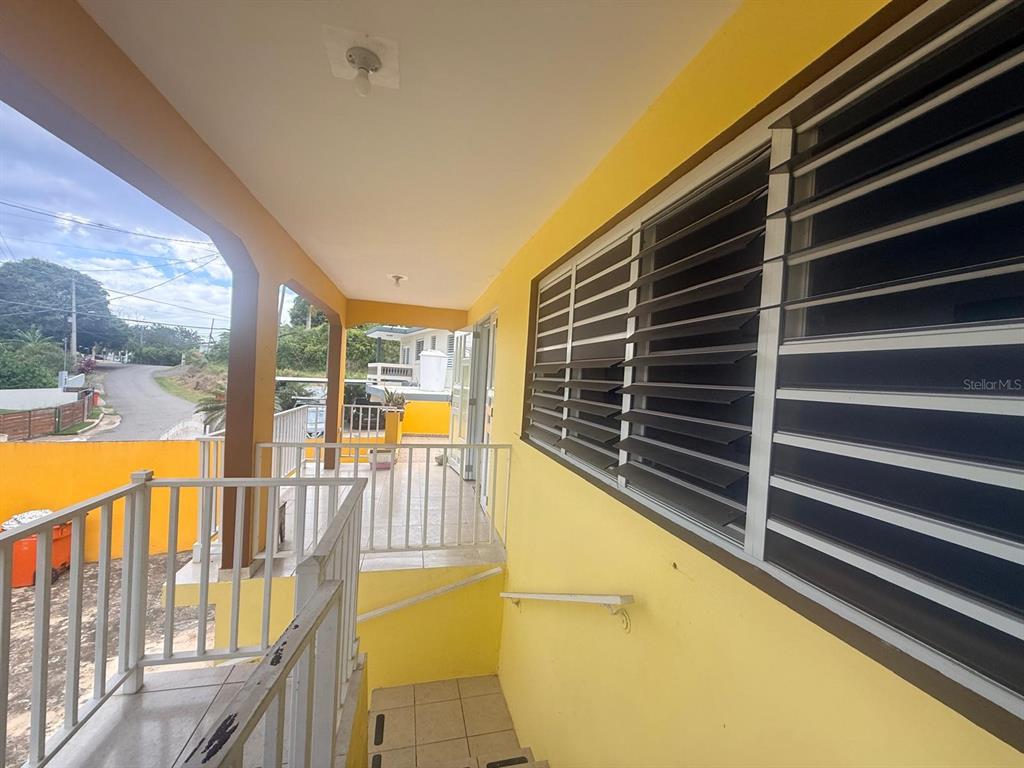 A yellow exterior balcony features a white metal railing and louvered windows — Carr. 411, Km. 0.2 LOS POZOS, SECTOR CALVACHE, RINCON, PR