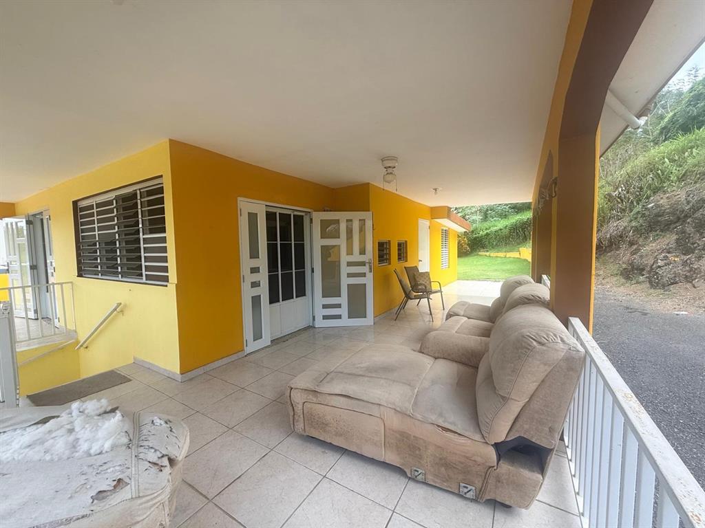 A covered patio features yellow walls, tiled floors, a large sofa, and a metal railing — Carr. 411, Km. 0.2 LOS POZOS, SECTOR CALVACHE, RINCON, PR