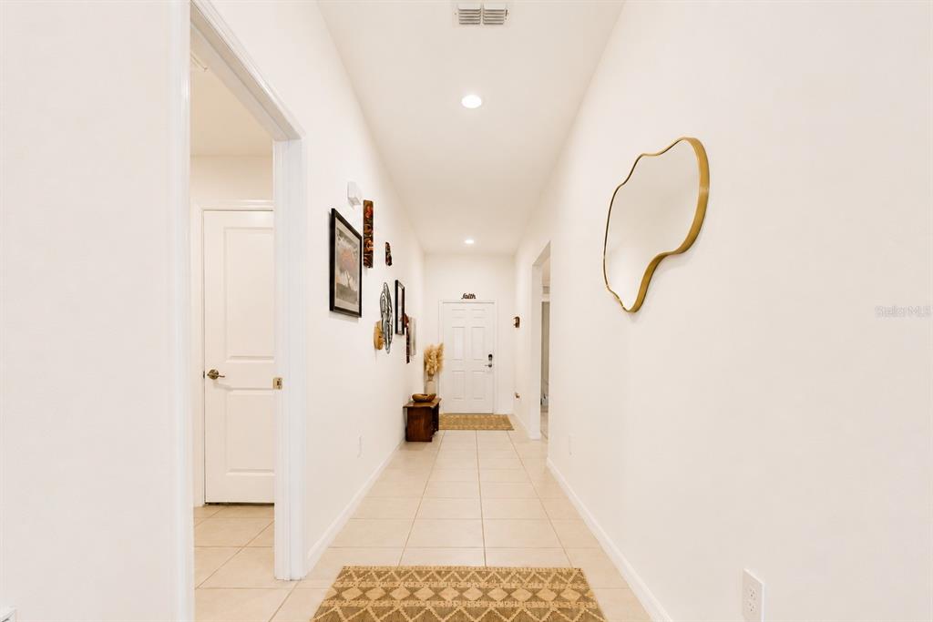 A bright hallway with tile flooring, white walls, a gold-framed mirror, and a front door — 13191 GARNET RASPBERRY AVENUE, WIMAUMA, FL