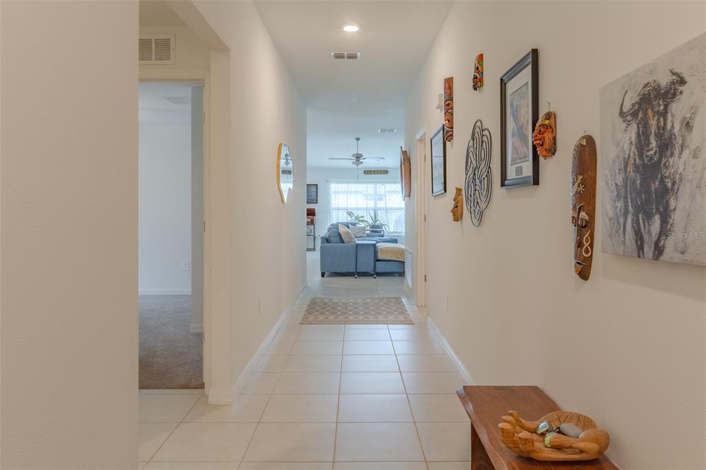 A tiled hallway leads from a foreground entryway toward a living room with a sofa — 13191 GARNET RASPBERRY AVENUE, WIMAUMA, FL