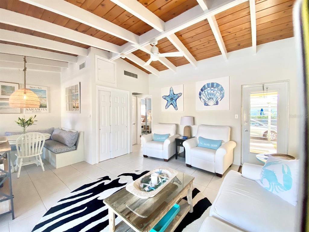 A living room features a wood-beamed ceiling, tile floors, white furniture, and coastal wall art — 6006 MIDNIGHT PASS ROAD UNIT 71, SARASOTA, FL