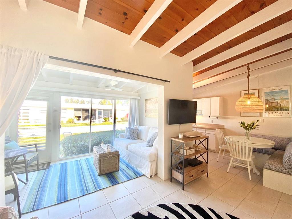 An open-concept living and dining area features white tile floors and exposed wood ceiling beams — 6006 MIDNIGHT PASS ROAD UNIT 71, SARASOTA, FL