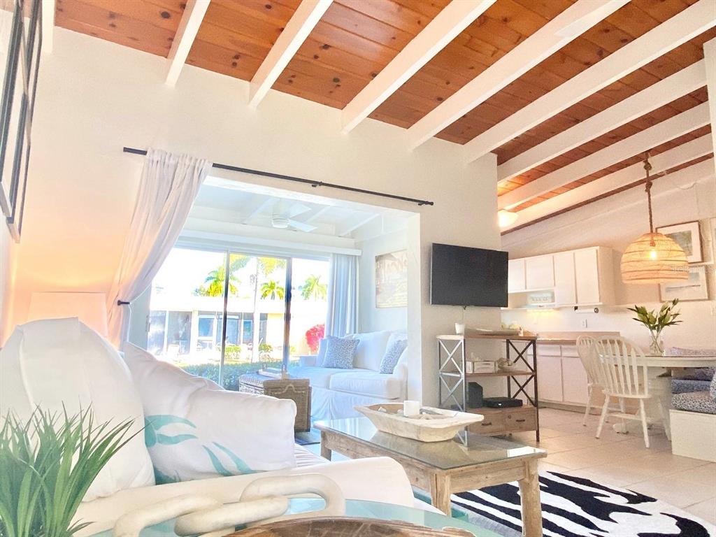 A living room with vaulted wood-beam ceilings, white furniture, and an adjacent dining area — 6006 MIDNIGHT PASS ROAD UNIT 71, SARASOTA, FL