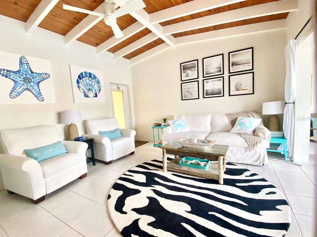 A bright living room features a zebra-print rug, white furniture, and a wood-beamed ceiling — 6006 MIDNIGHT PASS ROAD UNIT 71, SARASOTA, FL