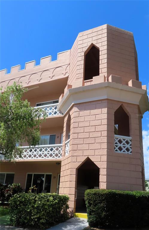 A three-story pink apartment building features a prominent corner tower with arched openings and battlements — 2457 ECUADORIAN WAY UNIT 85, CLEARWATER, FL