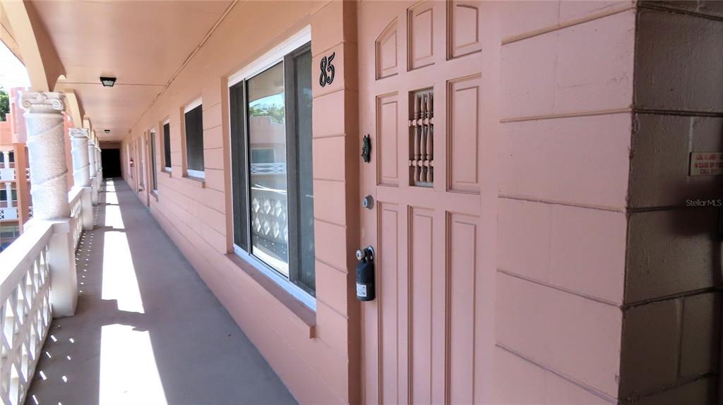An exterior walkway with peach-colored walls leads to a door marked with the number 85 — 2457 ECUADORIAN WAY UNIT 85, CLEARWATER, FL