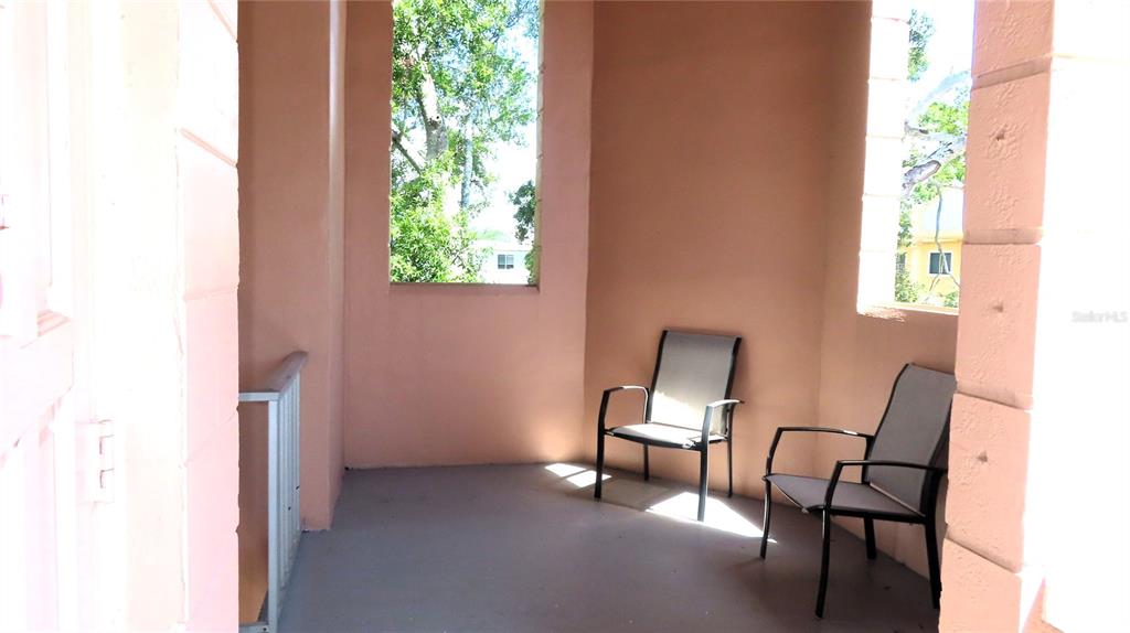 An outdoor balcony features peach-colored walls, a gray floor, and two metal patio chairs — 2457 ECUADORIAN WAY UNIT 85, CLEARWATER, FL