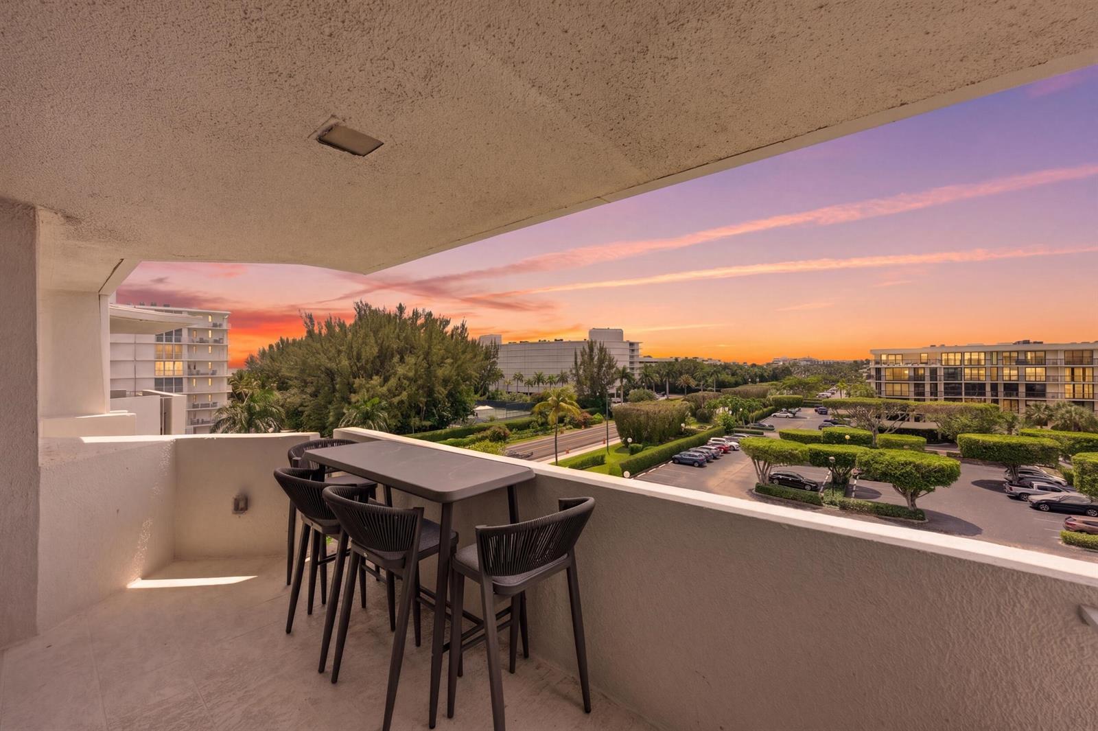 A balcony with a high-top table and chairs overlooks a parking lot at sunset — 2773 S Ocean Boulevard # 5140, Palm Beach FL 33480, PALM BEACH, FL