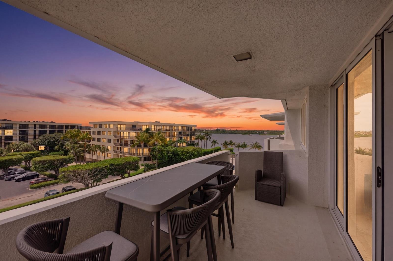 A balcony with a dining set overlooks a parking lot, palm trees, and a sunset — 2773 S Ocean Boulevard # 5140, Palm Beach FL 33480, PALM BEACH, FL