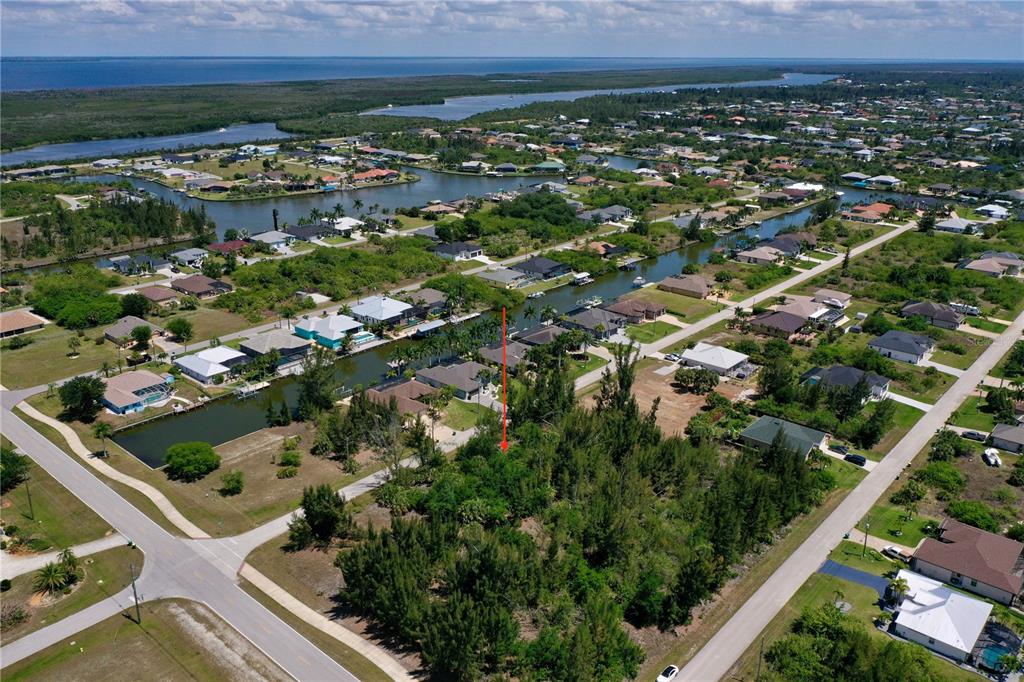 An aerial view shows a vacant, tree-covered lot marked by a red arrow near canals — 8401 ANTWERP CIRCLE, PORT CHARLOTTE, FL