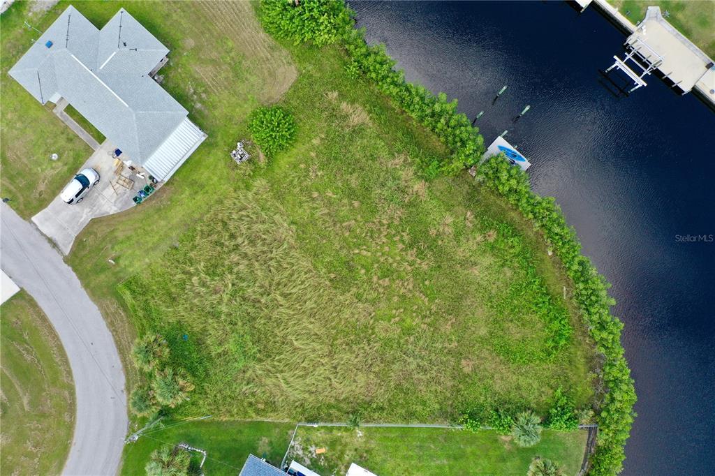An aerial view shows a vacant, grassy waterfront lot next to a house and canal — 18106 AVONSDALE CIRCLE, PORT CHARLOTTE, FL
