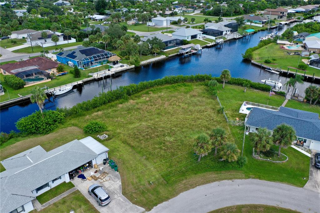 An aerial view shows a vacant grassy lot situated between two houses along a canal — 18106 AVONSDALE CIRCLE, PORT CHARLOTTE, FL