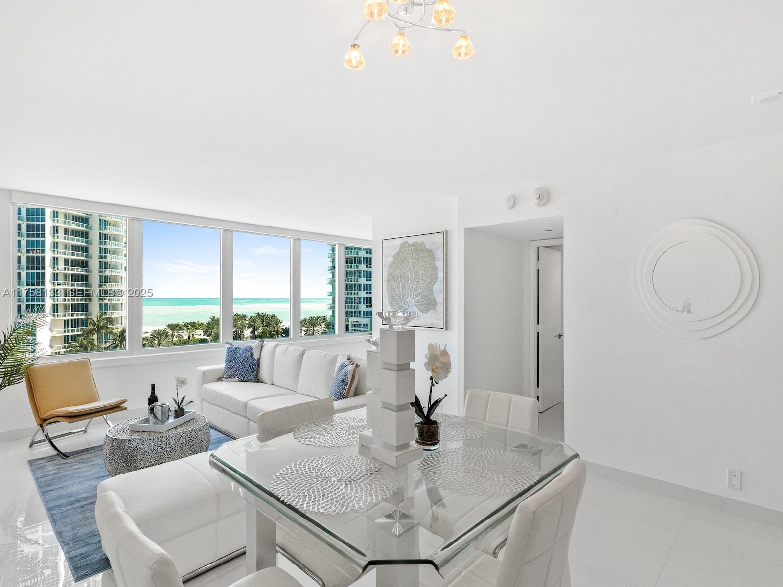 A bright living and dining area features white furniture, a glass table, and ocean views — 400 S Pointe Dr # 906, Miami Beach FL 33139, MIAMI BEACH, FL