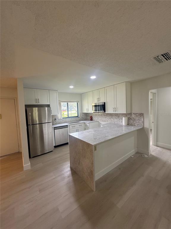 A kitchen features white cabinetry, stainless steel appliances, a marble-patterned peninsula, and light wood flooring — 10719 LAZY LAKE DRIVE, ORLANDO, FL