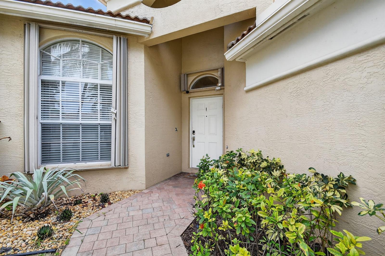 The exterior view shows a beige stucco home entrance with a white door and walkway — 2544 Sandy Cay, West Palm Beach FL 33411, WEST PALM BEACH, FL