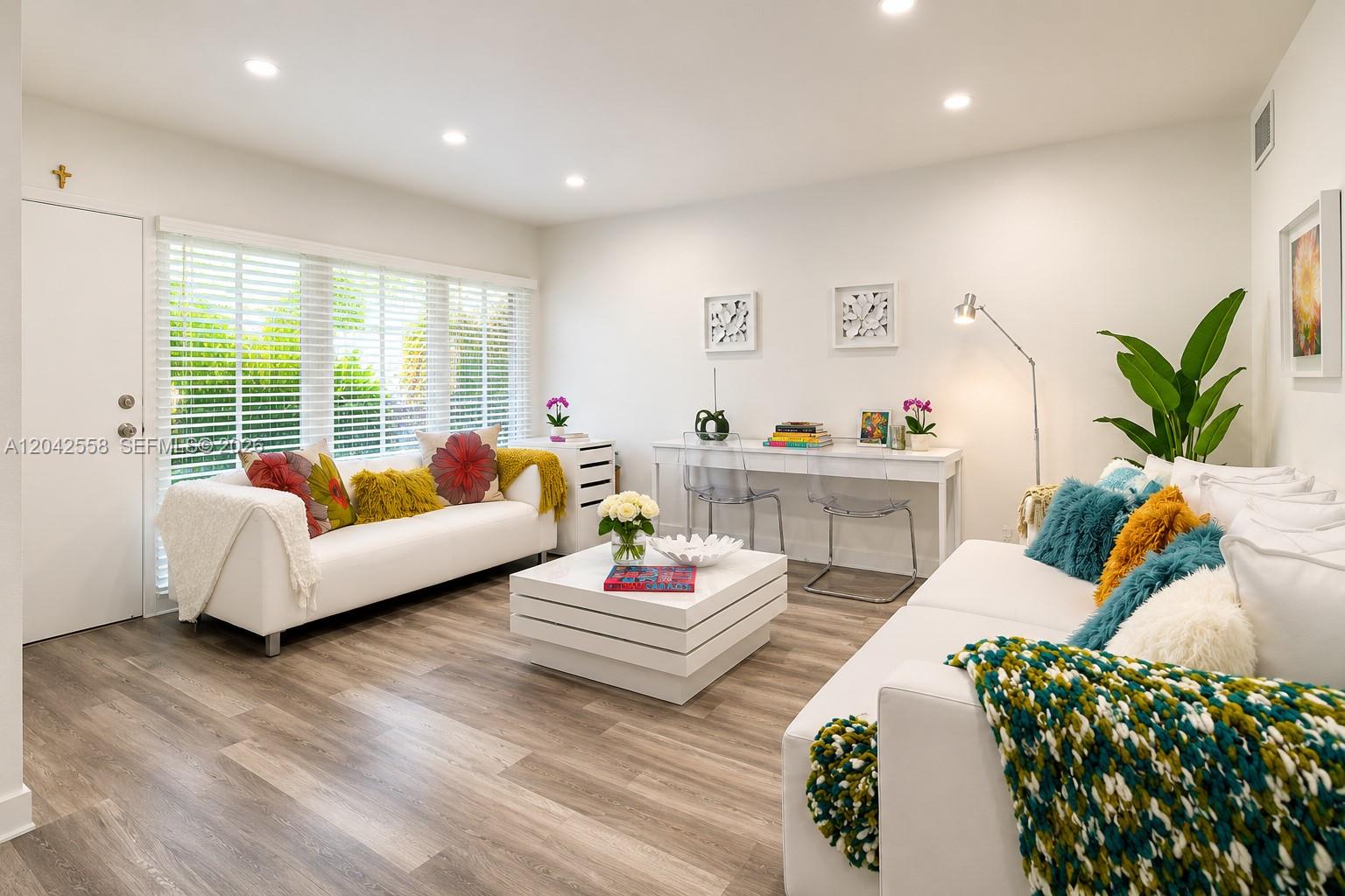 A bright living room features white sofas, a tiered coffee table, and a desk area — 35 Edgewater Dr # 107, Coral Gables FL 33133, CORAL GABLES, FL