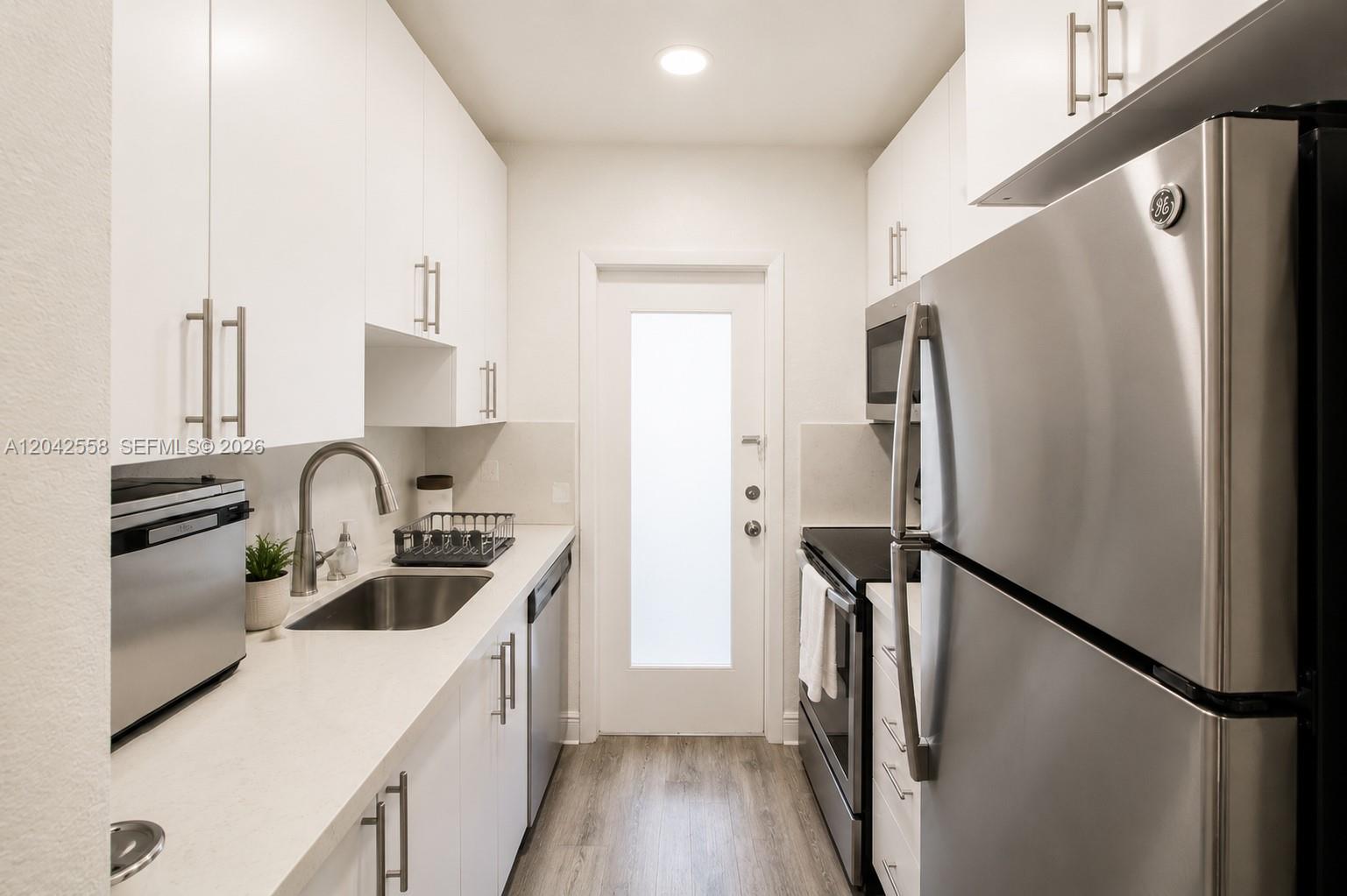 A galley kitchen features white cabinets, stainless steel appliances, and light wood-look flooring — 35 Edgewater Dr # 107, Coral Gables FL 33133, CORAL GABLES, FL