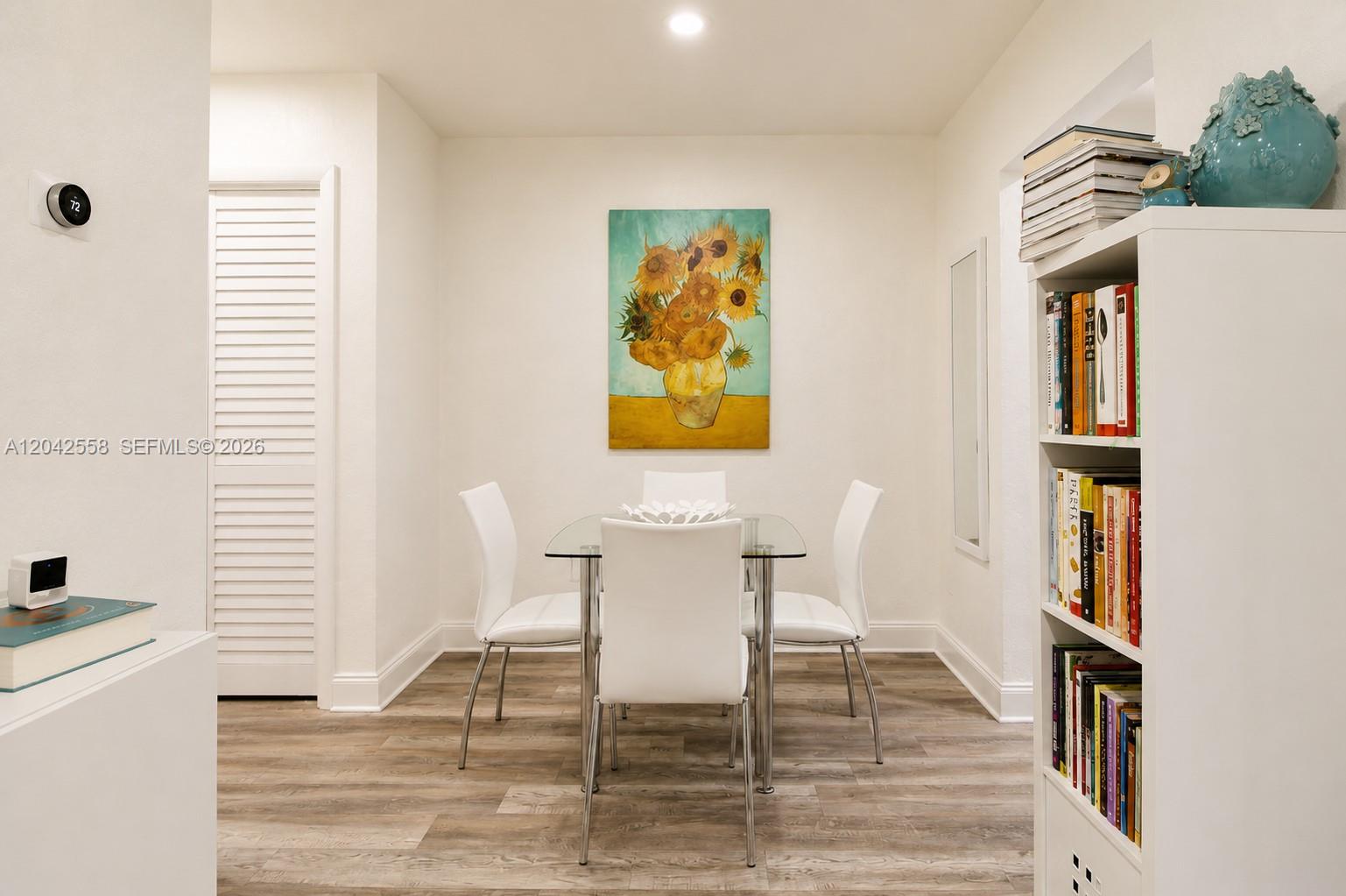 A dining area features a glass table, four white chairs, and a sunflower painting — 35 Edgewater Dr # 107, Coral Gables FL 33133, CORAL GABLES, FL