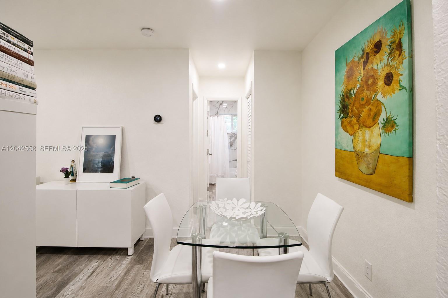 A dining area features a glass table, four white chairs, and a sunflower painting — 35 Edgewater Dr # 107, Coral Gables FL 33133, CORAL GABLES, FL