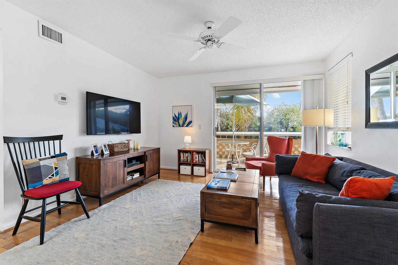 A living room with hardwood floors, a dark sofa, a television, and a sliding glass door — 353 S Us Hwy 1 # C7, Jupiter FL 33477, JUPITER, FL