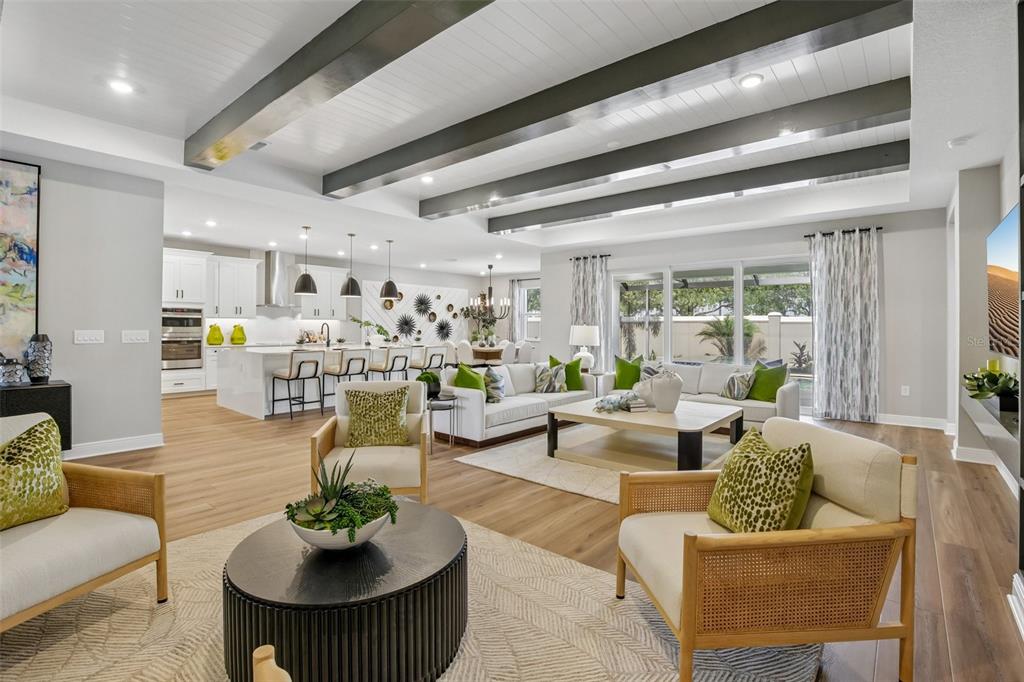 An open-concept living room and kitchen featuring dark ceiling beams and light wood flooring — 8924 DEEP HORIZON LOOP, PARRISH, FL