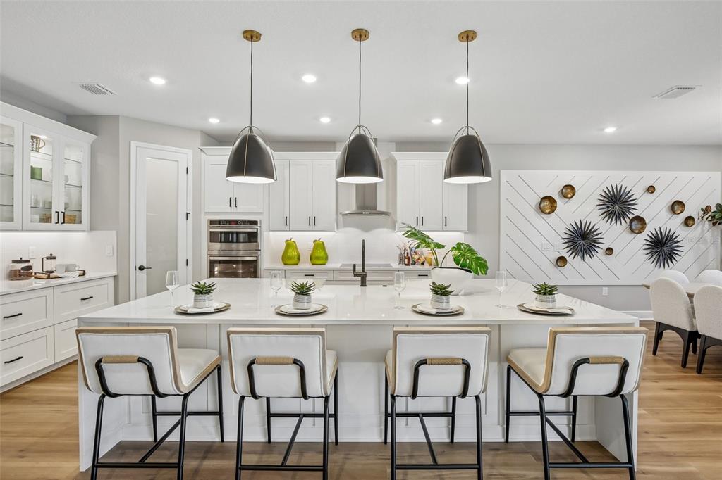 A modern kitchen features a large white island, pendant lighting, and white cabinetry — 8924 DEEP HORIZON LOOP, PARRISH, FL
