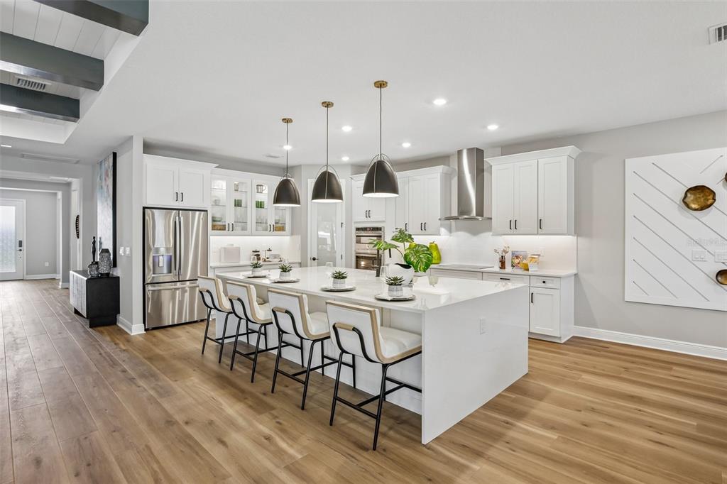A modern kitchen features white cabinetry, a large quartz island with seating, and wood flooring — 8924 DEEP HORIZON LOOP, PARRISH, FL