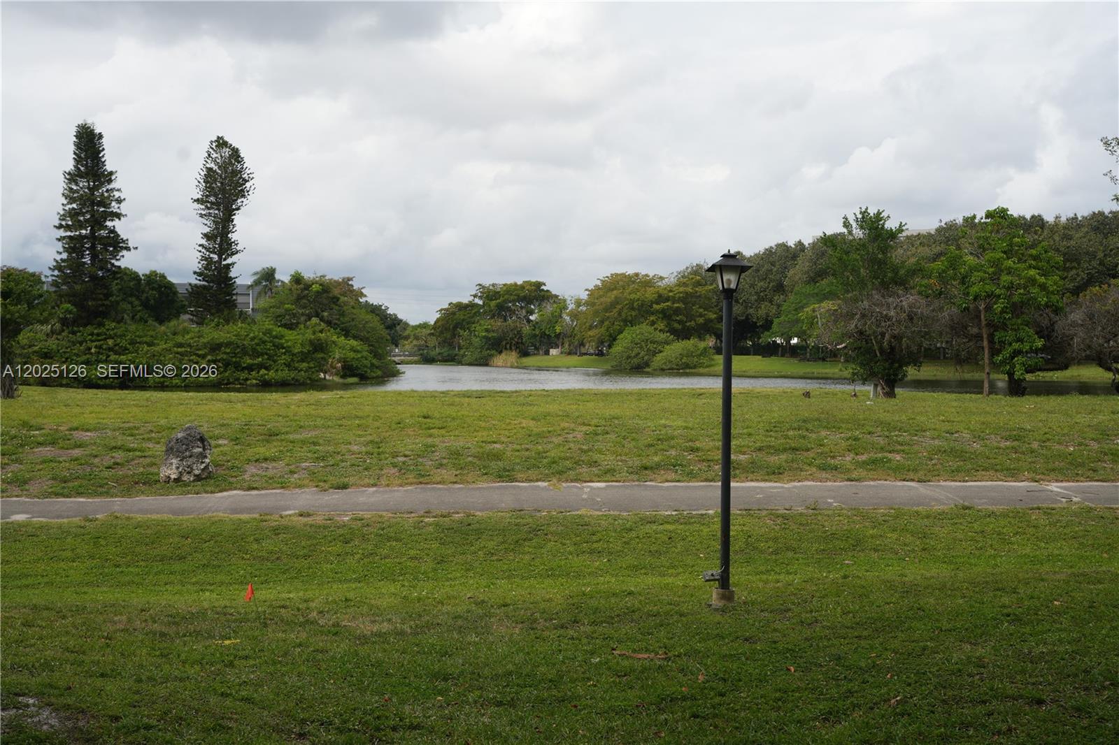A grassy lawn with a path and lamp post overlooks a pond and trees — 6001 N Falls Cir Dr # 203, Lauderhill FL 33319, LAUDERHILL, FL