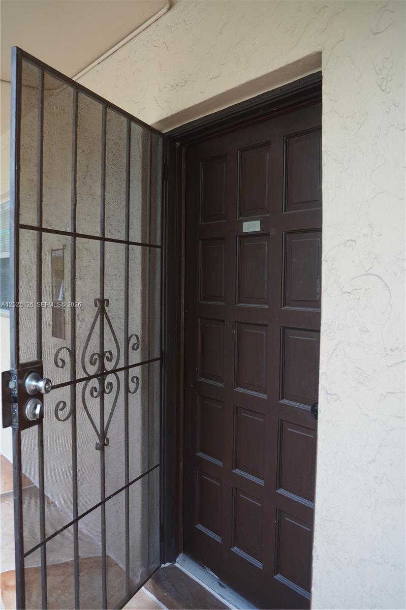 A brown paneled door with a decorative metal security screen stands in a stucco entryway — 6001 N Falls Cir Dr # 203, Lauderhill FL 33319, LAUDERHILL, FL