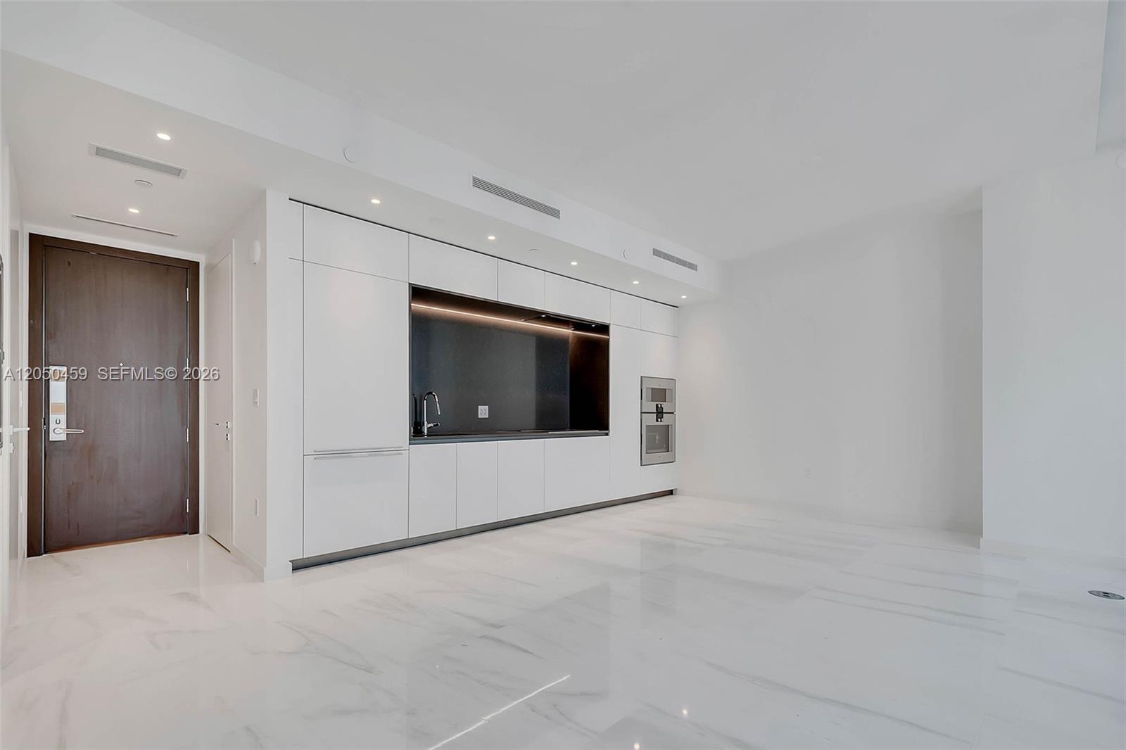 A minimalist kitchen features white cabinetry, a dark backsplash, and polished marble flooring — 300 Biscayne Boulevard Way # 3008W, Miami FL 33131, MIAMI, FL