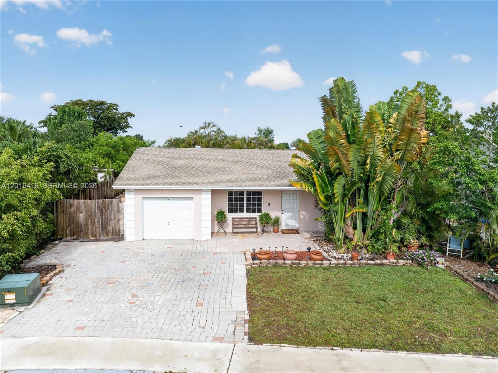 A single-story house with a paved driveway, a garage, and large tropical plants — 9600 Richmond Cir, Boca Raton FL 33434, BOCA RATON, FL