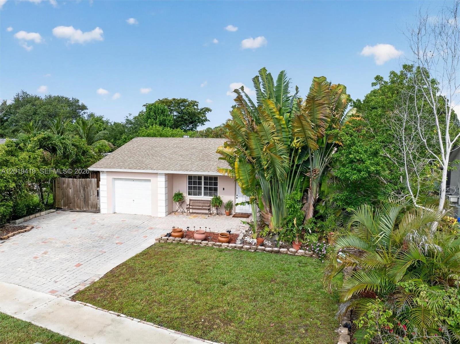 A single-story house with a paved driveway, garage, and large tropical plants in the front yard — 9600 Richmond Cir, Boca Raton FL 33434, BOCA RATON, FL