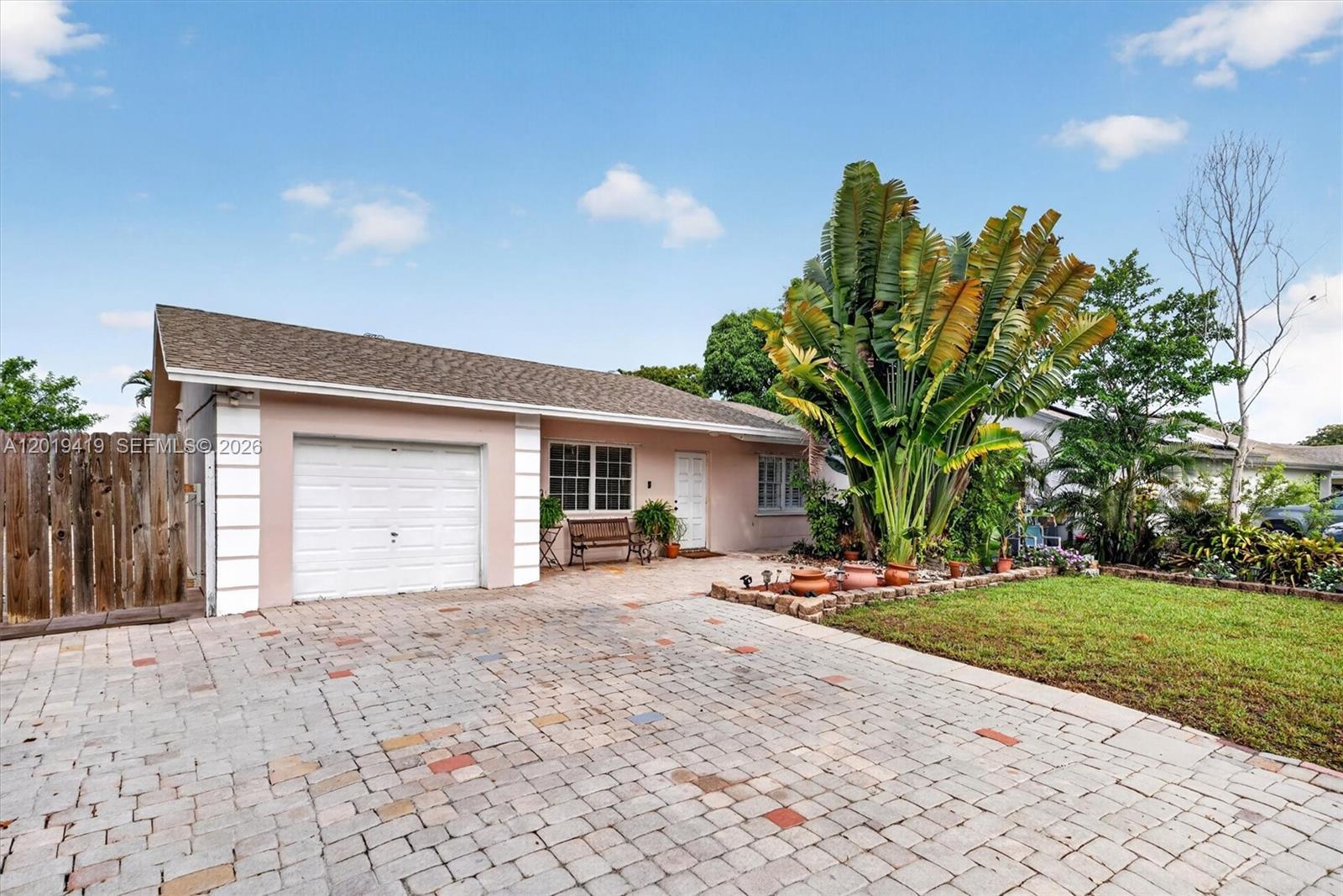 A single-story house with a white garage door, paved driveway, and large tropical plants — 9600 Richmond Cir, Boca Raton FL 33434, BOCA RATON, FL