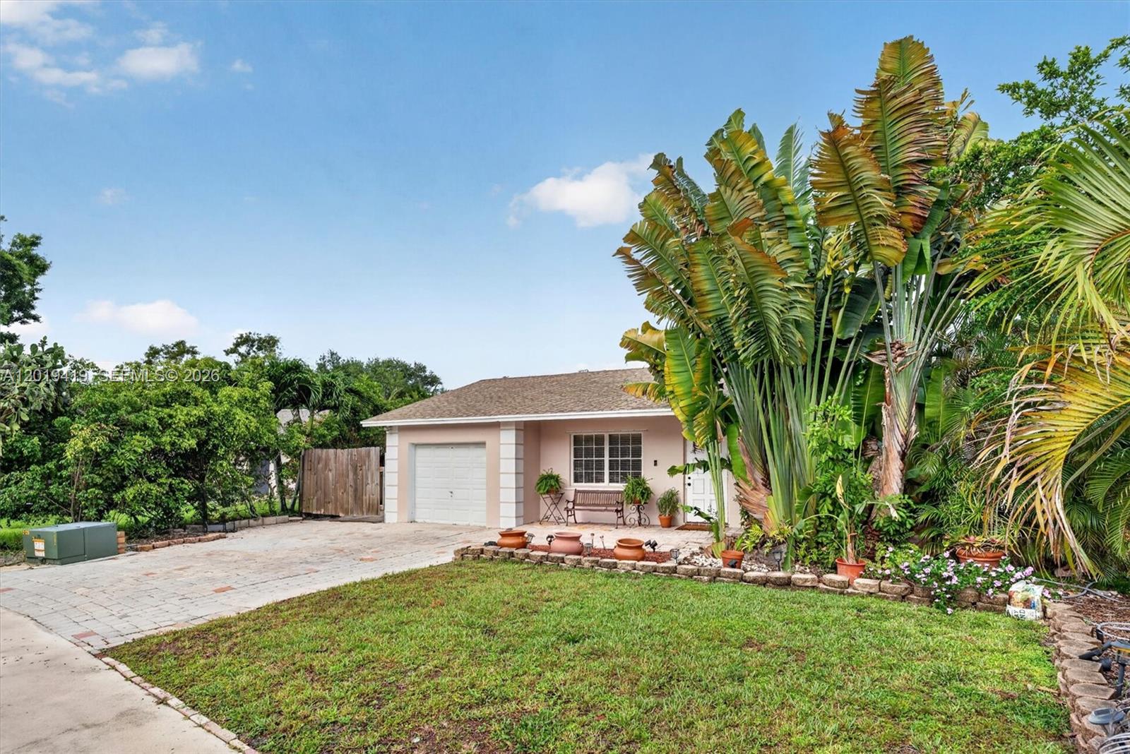 A single-story house with a garage, a paved driveway, and large tropical plants in front — 9600 Richmond Cir, Boca Raton FL 33434, BOCA RATON, FL