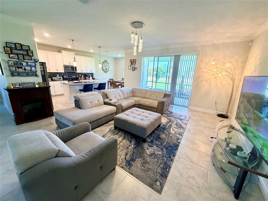 An open-concept living room features a sectional sofa, a fireplace, and an adjacent kitchen — 2572 CAMDEN PARK CIRCLE, DAVENPORT, FL
