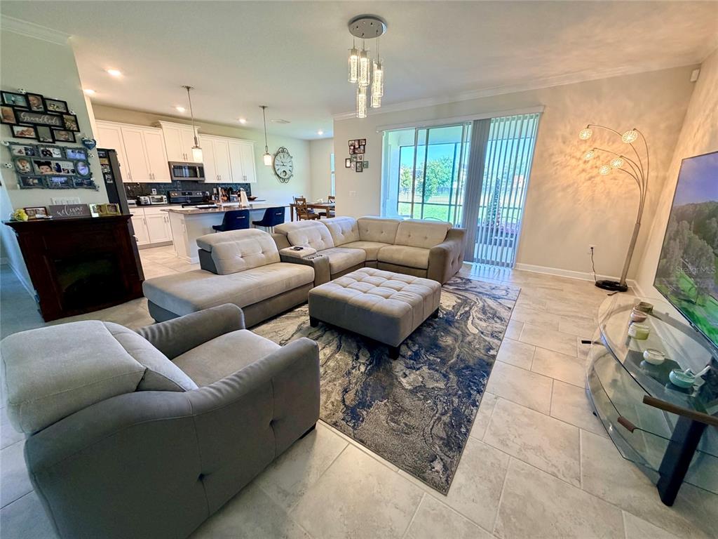 An open-concept living room features a sectional sofa, a central ottoman, and a kitchen area — 2572 CAMDEN PARK CIRCLE, DAVENPORT, FL