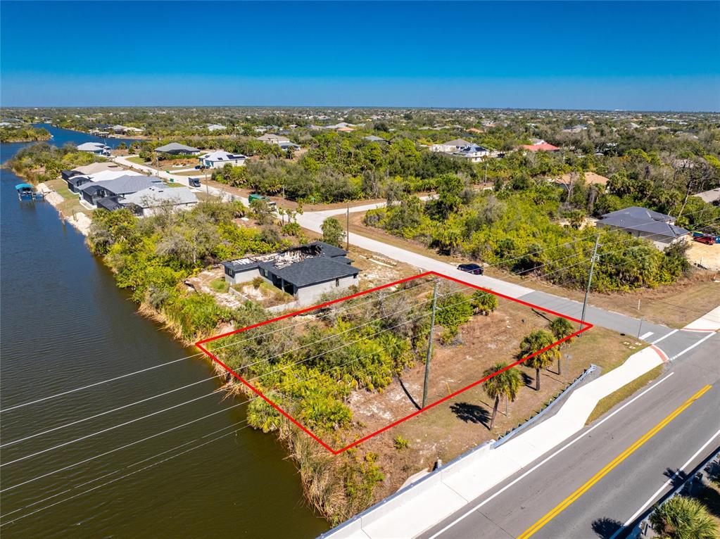 An aerial view shows a vacant, rectangular waterfront lot outlined in red next to a road — 10311 REDONDO STREET, PORT CHARLOTTE, FL