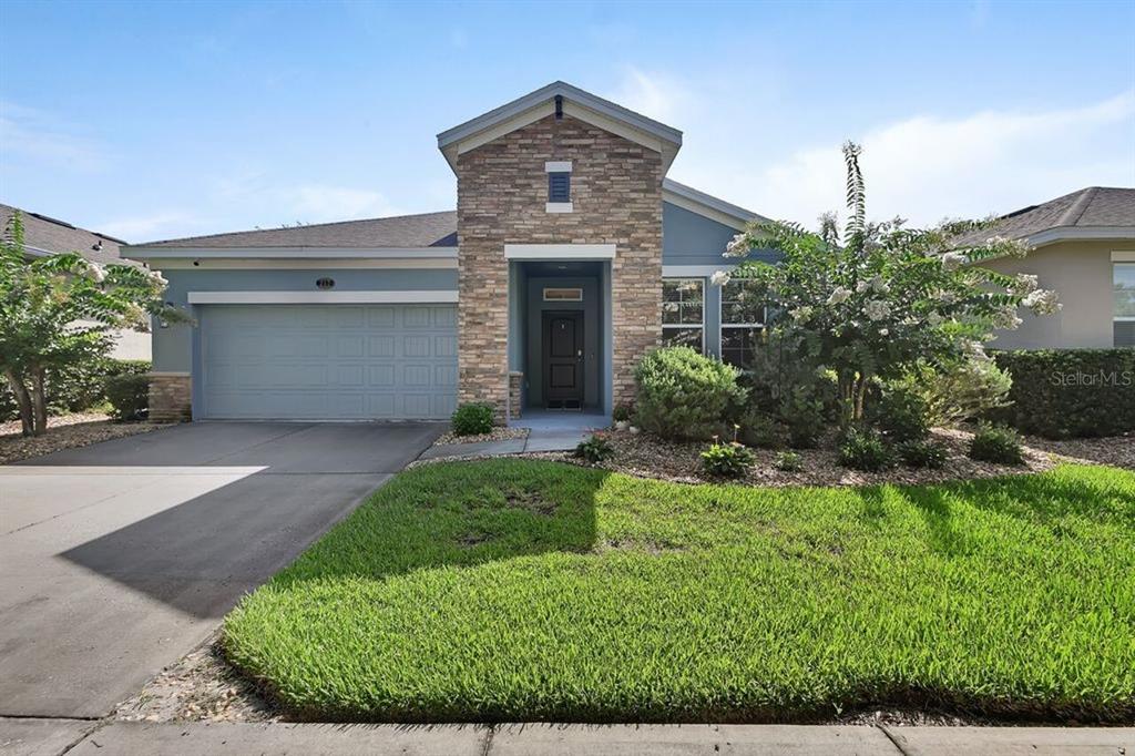 A single-story house with a stone-accented entryway, blue siding, a two-car garage, and landscaping — 217 W CHERRY PLACE, DELAND, FL