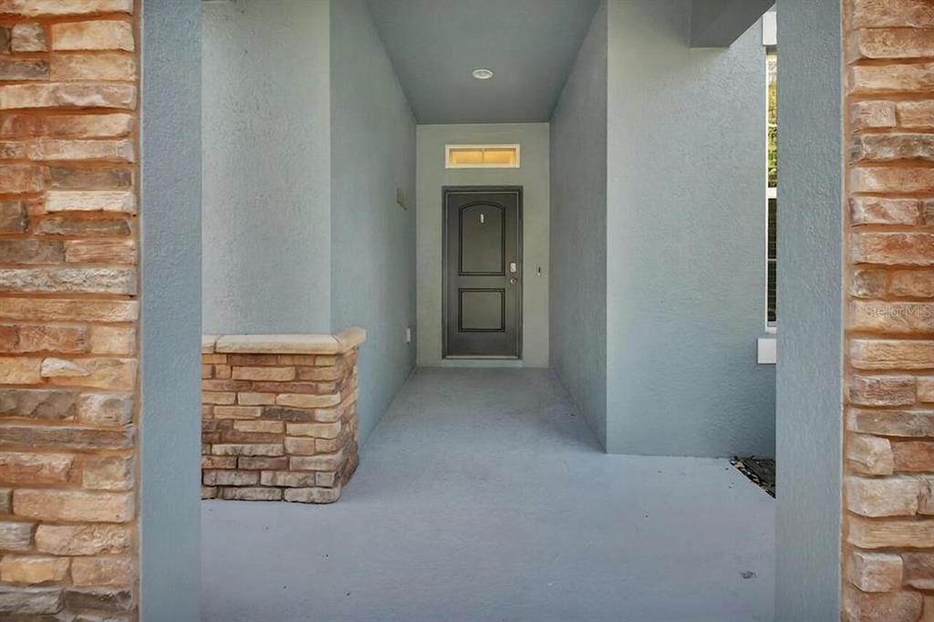 A covered entryway features a dark front door, light blue walls, and stone veneer accents — 217 W CHERRY PLACE, DELAND, FL