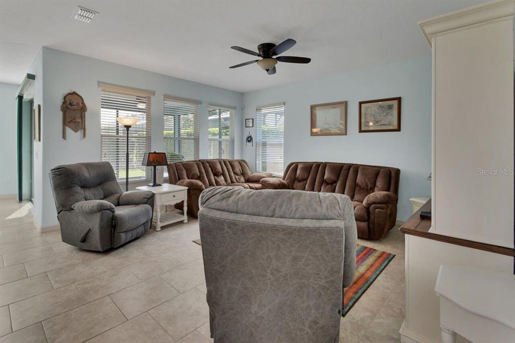 A living room features light blue walls, tile flooring, a ceiling fan, and brown furniture — 217 W CHERRY PLACE, DELAND, FL