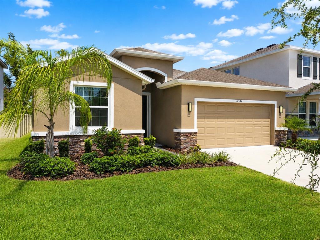 A single-story suburban house with a tan stucco exterior, stone accents, and a two-car garage — 12544 SHINING WILLOW STREET, RIVERVIEW, FL