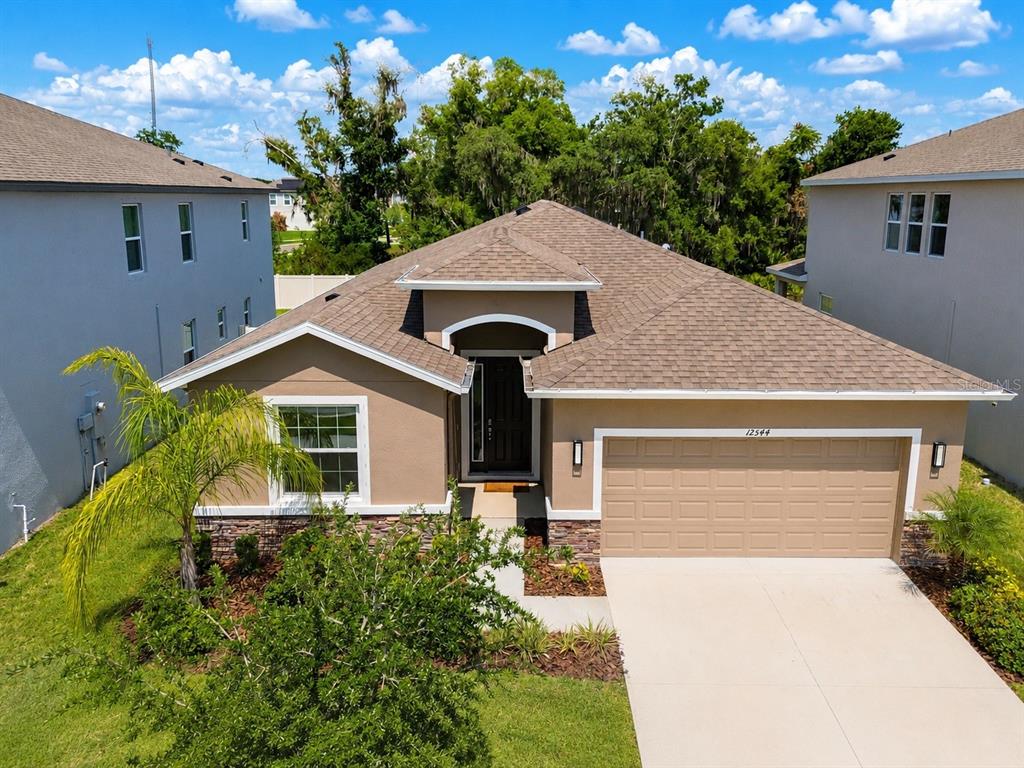 An exterior view of a single-story suburban house with a tan facade and garage — 12544 SHINING WILLOW STREET, RIVERVIEW, FL