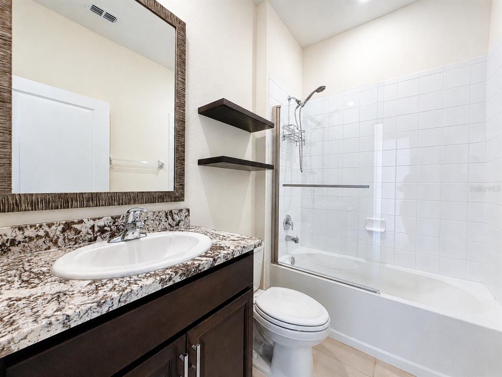 A bathroom features a granite vanity, dark wood cabinets, a mirror, and a shower-tub combo — 12544 SHINING WILLOW STREET, RIVERVIEW, FL