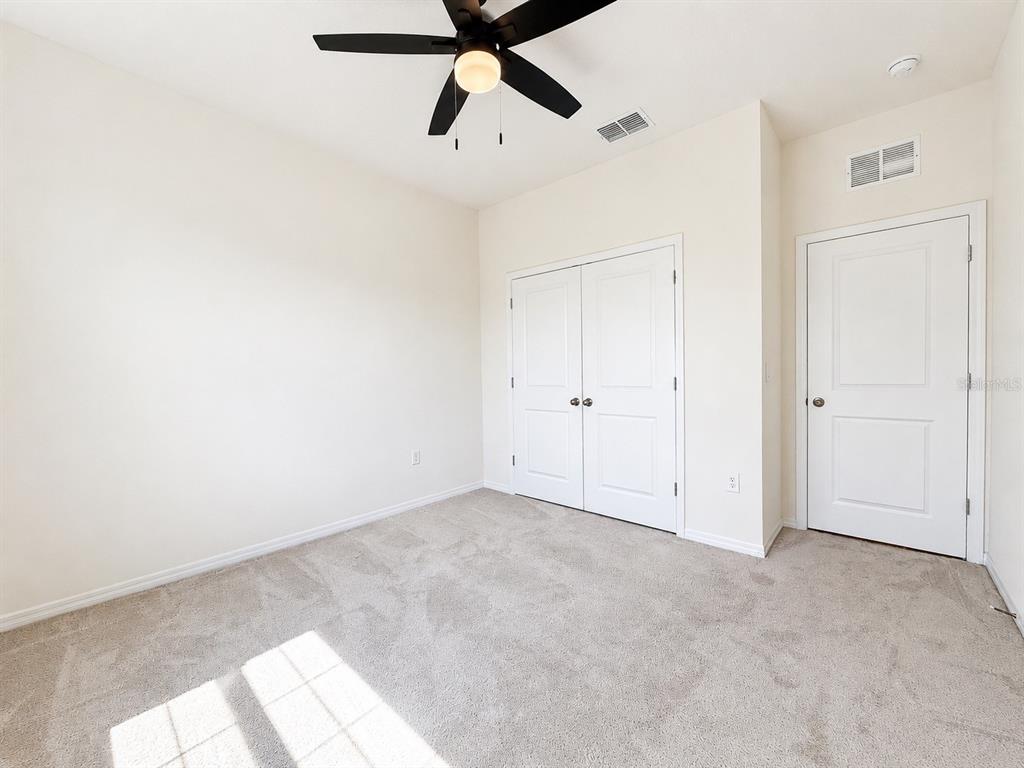 An empty bedroom features beige carpet, white walls, a ceiling fan, and two white doors — 12544 SHINING WILLOW STREET, RIVERVIEW, FL